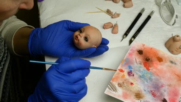 Faire des poupées. Maître marionnette peint intensément les lèvres de blanc pour poupée avec un pinceau mince. Concept de création de poupées artisanales . — Video