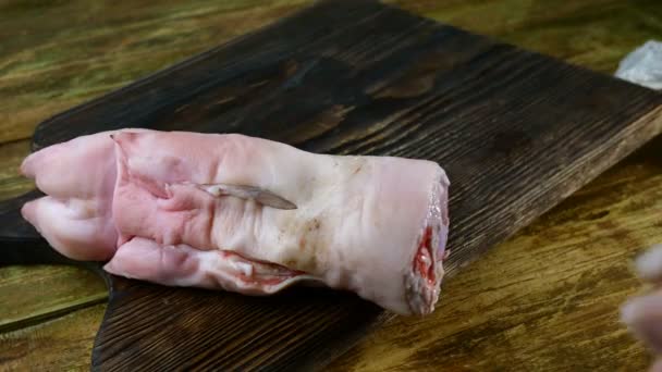 Préparation cuisses de porc. Pas à pas. Les mains humaines dans des gants en caoutchouc mettent soigneusement les jambes de porc crues sur le panneau de cuisine en bois. Gros plan . — Video