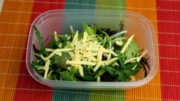 Laitue, rucola et autres herbes au fromage râpé versé avec de l'huile de cuisson et mettre une boîte à lunch en plastique et décorer de fleurs de casserole. Gros plan . — Video