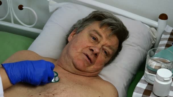 Lekarz słucha stetoskopem serca i płuc udręczonego chorego człowieka rasy kaukaskiej, który leży na łóżku w szpitalu lub w domu. Zbliżenie. — Wideo stockowe