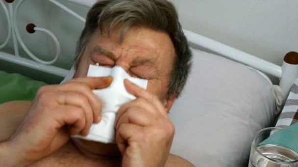 Tormented sick caucasian Ethnicity man, sneezes into napkin, is lying on bed in hospital or at home. Close-up. — Stock Video