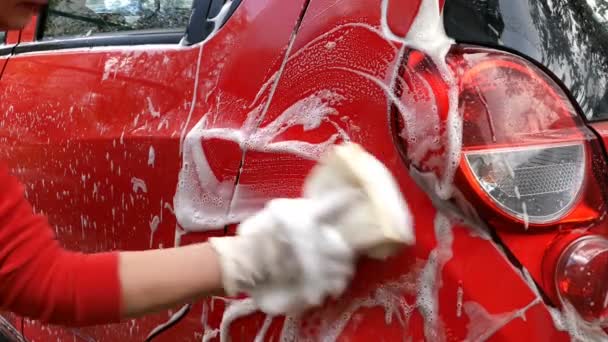 Γυναίκα με κόκκινα ρούχα πλένει βρώμικο κόκκινο αυτοκίνητο με το χέρι με σφουγγάρι και σαπουνόφουσκα. Στην πίσω αυλή του σπιτιού της. Κλείσε.. — Αρχείο Βίντεο