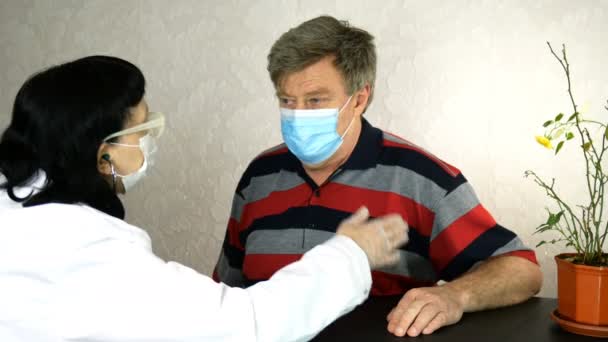 Sympathetically doctor listens with stethoscope to heart and lungs of a tormented sick caucasian Ethnicity man in medical mask, who sits by table in hospital or at home. Close up. — Stock Video