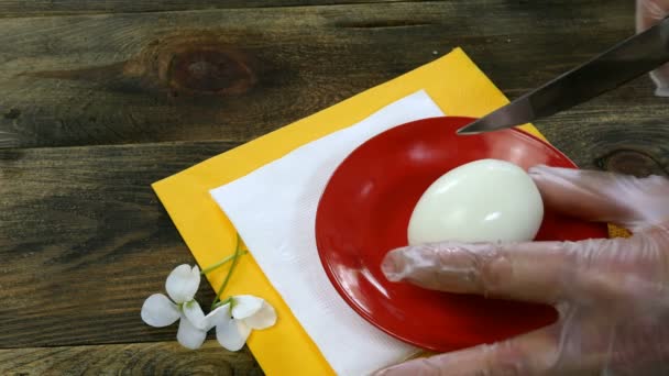 Human hands cut boiled egg with kitchen knife on wooden table. Close-up. — Stock Video