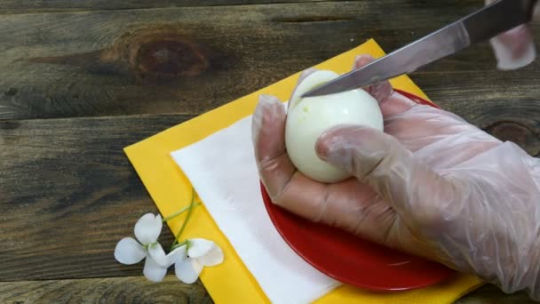 Menschliche Hände schneiden gekochtes Ei mit einem Küchenmesser auf einen Holztisch. Nahaufnahme. — Stockvideo