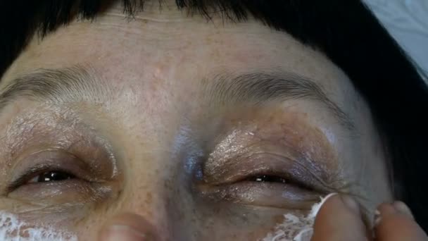 Volwassen volwassen vrouw, blanke etniciteit smeren hydraterende cosmetische crème rimpels op haar gezicht met vingers, op zoek naar camera. Close-up. — Stockvideo