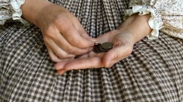 素朴なドレスで成熟した大人の女性のしわの手は、彼女の手の手のひらにいくつかの異なる小さなコインをカウントします。貧困と金融危機の概念。閉じろ!. — ストック動画