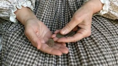 Kırsal giysili yetişkin bir kadının kırış kırış elleri avucunun içinde farklı küçük paralar sayıyor. Yoksulluk ve finansal kriz kavramı. Kapat..