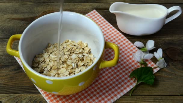 Vegetarian healthy breakfast with porridge. Oatmeal flakes in yellow bowl poured with water. On kitchen table. Close-up. — Stock Video