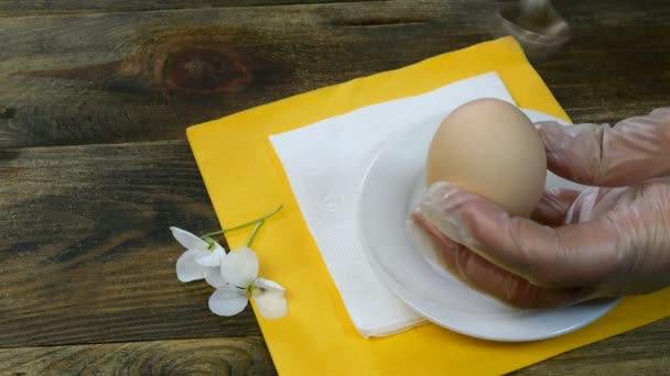 La persona toma un huevo hervido con las manos del platillo blanco, rompe la cáscara con cucharadita y pelando el huevo. Primer plano . — Vídeo de stock