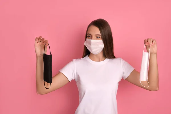Mutlu esmer kız Corona virüsünden korumak için beyaz bir maske takıyor. Elinde beyaz ve siyah bir maske tutuyor. Sağlığını ve güvenliğini düşünüyor.