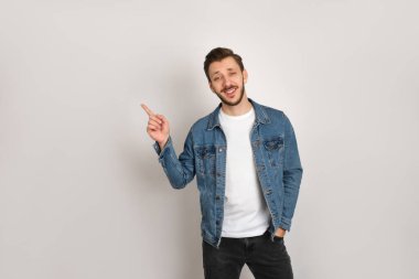 Kot ceketli ve beyaz tişörtlü yakışıklı hippi gri arka planda, kaşlarını çatmış ve gülümsüyor..