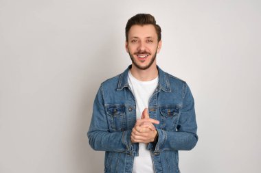 Kot ceketli ve beyaz tişörtlü yakışıklı hippi ellerini gri arka planda gezdiriyor, hafifçe gülümsüyor, rahatlamış hissediyor..