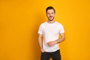 Sarı arka planda beyaz tişört giymiş yakışıklı bir adamın renkli portresi, bir eli cebinde, diğeri düz, kendinden emin..
