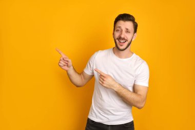 Beyaz tişörtlü yakışıklı bir adam portresi iki eli sarı arka planda, mutlu bir şekilde gülümsüyor, kendinden emin hissediyor..