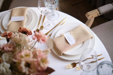 Restorandaki lüks sonbahar düğün masası dekorasyonu. Taze ve kuru çiçekler, güller, karanfiller. Güzel masa düzenleme: Altın eşyalar, çatal ve bıçak, kaligrafi misafir oturma kartı.