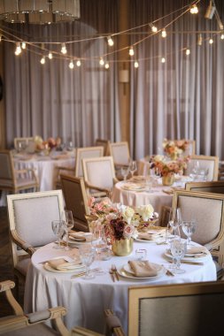 Restorandaki lüks sonbahar düğün masası dekorasyonu. Taze ve kuru çiçekler, güller, karanfiller. Güzel masa düzenleme: Altın eşyalar, çatal ve bıçak, kaligrafi misafir oturma kartı.