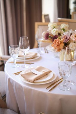 Restorandaki lüks sonbahar düğün masası dekorasyonu. Taze ve kuru çiçekler, güller, karanfiller. Güzel masa düzenleme: Altın eşyalar, çatal ve bıçak, kaligrafi misafir oturma kartı.