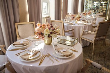 Restorandaki lüks sonbahar düğün masası dekorasyonu. Taze ve kuru çiçekler, güller, karanfiller. Güzel masa düzenleme: Altın eşyalar, çatal ve bıçak, kaligrafi misafir oturma kartı.