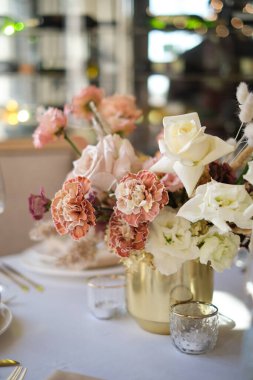 Restorandaki lüks sonbahar düğün masası dekorasyonu. Taze ve kuru çiçekler, güller, karanfiller. Güzel masa düzenleme: Altın eşyalar, çatal ve bıçak, kaligrafi misafir oturma kartı.