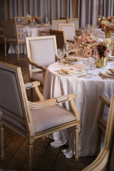 Luxury cozy autumn wedding table decoration in the restaurant. Fresh and dried flowers, roses, carnations. Beautiful table setting: golden appliances, fork and knife, calligraphy guest seating card.