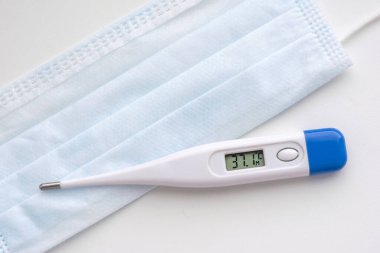 Sıcaklık numarası 37.1 olan termometre beyaz arka planda mavi bir tıbbi maske takıyor. Coronavirus Önlemleri Maske Koruması.