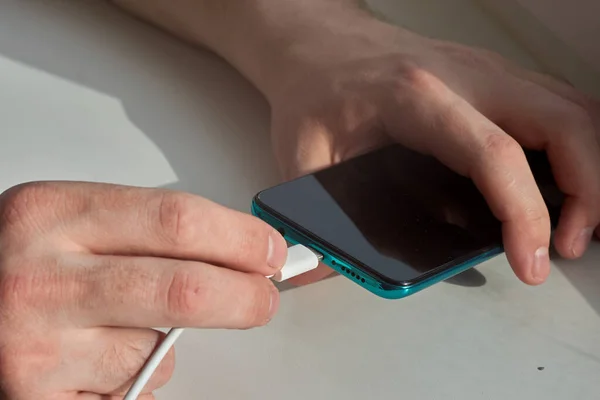 Adam akıllı bir telefonun şarj aletini fişe takıyor.