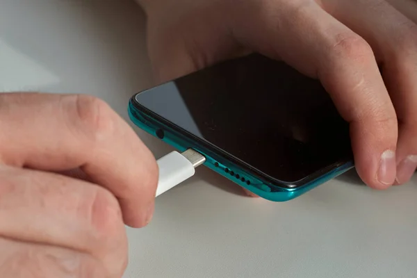 Adam akıllı bir telefonun şarj aletini fişe takıyor.