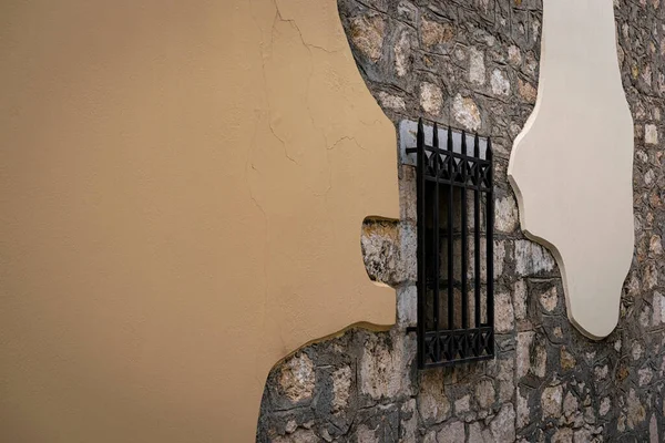 Taş bir duvarda metal parmaklıklı pencere stil ve renklerle.