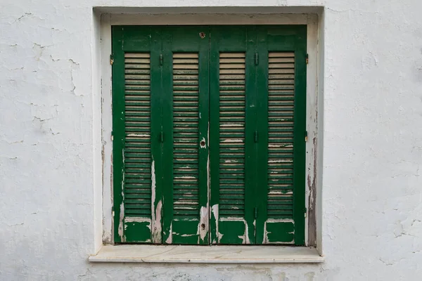 Old classic traditional square window with green shutters on an old white exterior wall with texture.