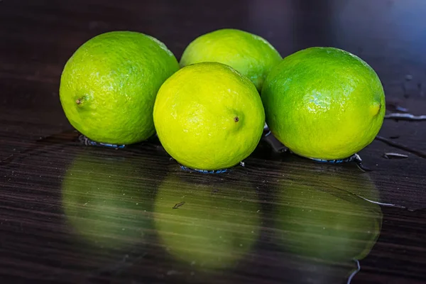 Tahta bir yüzeyde yansımaları olan dört taze limon..
