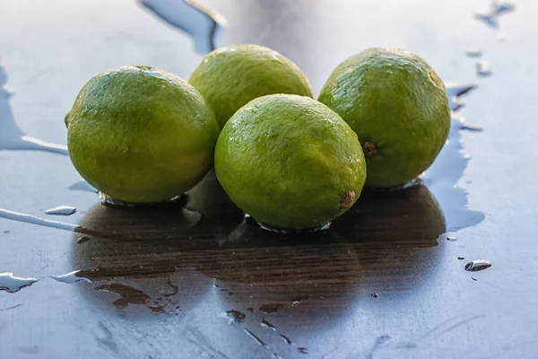 Islak bir yüzeyde yansımaları olan dört yeşil taze limon..