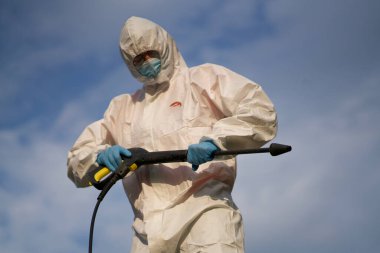 Beyaz elbiseli bir adam, mikroplu bölgeyi koronavirüs virüsü ile dezenfekte ediyor, iş yerinde fotoğraf çekiliyor, arka plandan çekiliyor, yeşil, mesaj için boş alan var.