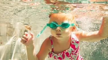 Havuzda yüzen mayo ve gözlüklü küçük kız. 