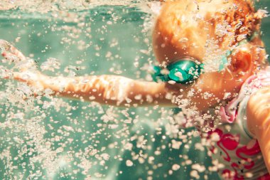 Havuzda yüzen mayo ve gözlüklü küçük kız. 