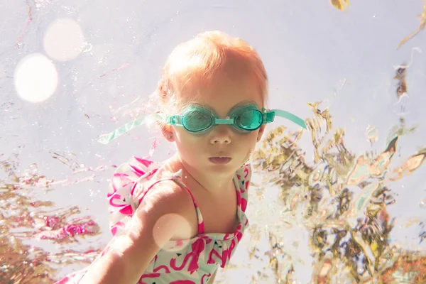 穿着泳衣和眼镜的小女孩在游泳池里游泳 — 图库照片