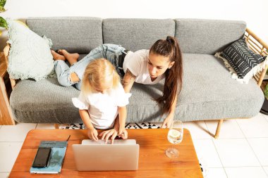 Güzel, genç bir bayan, arka planda küçük bir kızla evde çalışıyor.