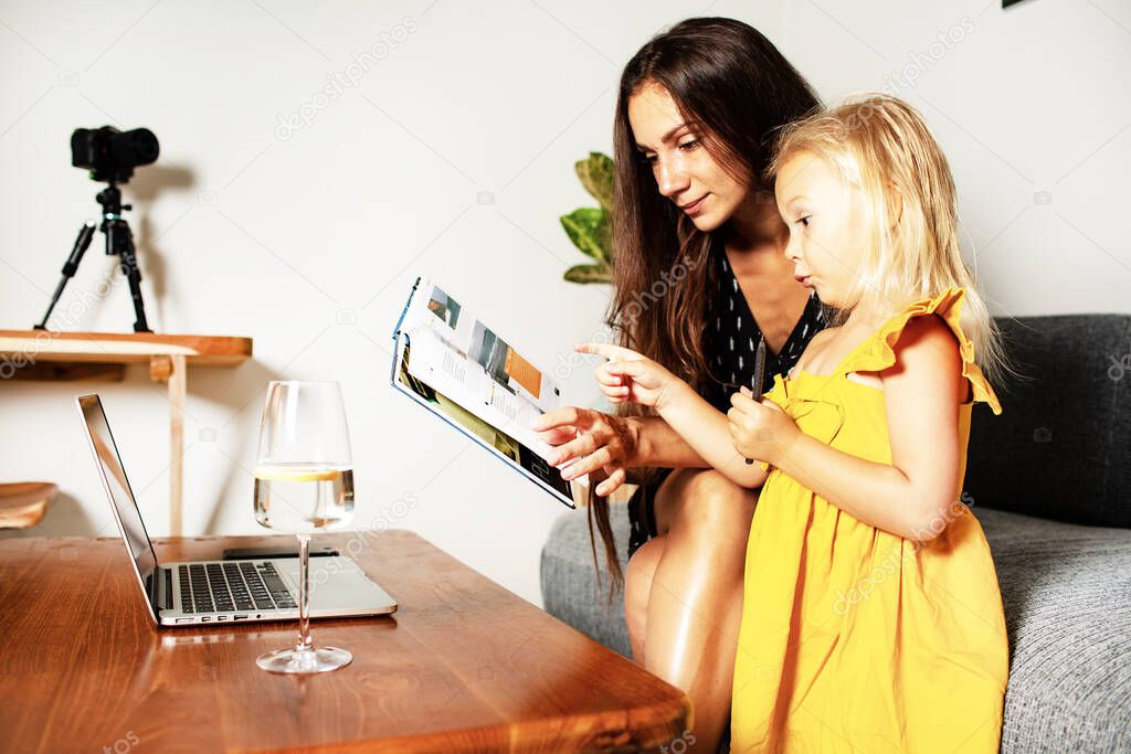 beautiful young female working at home with little kid girl in room background