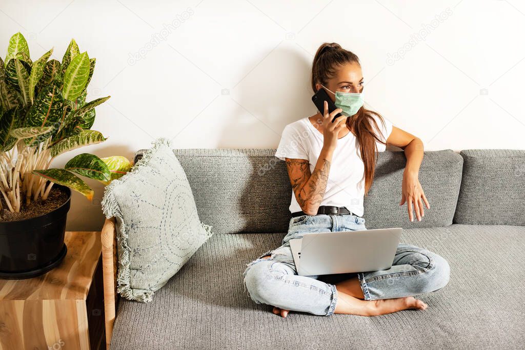 young woman working at home in face mask in room sofa background