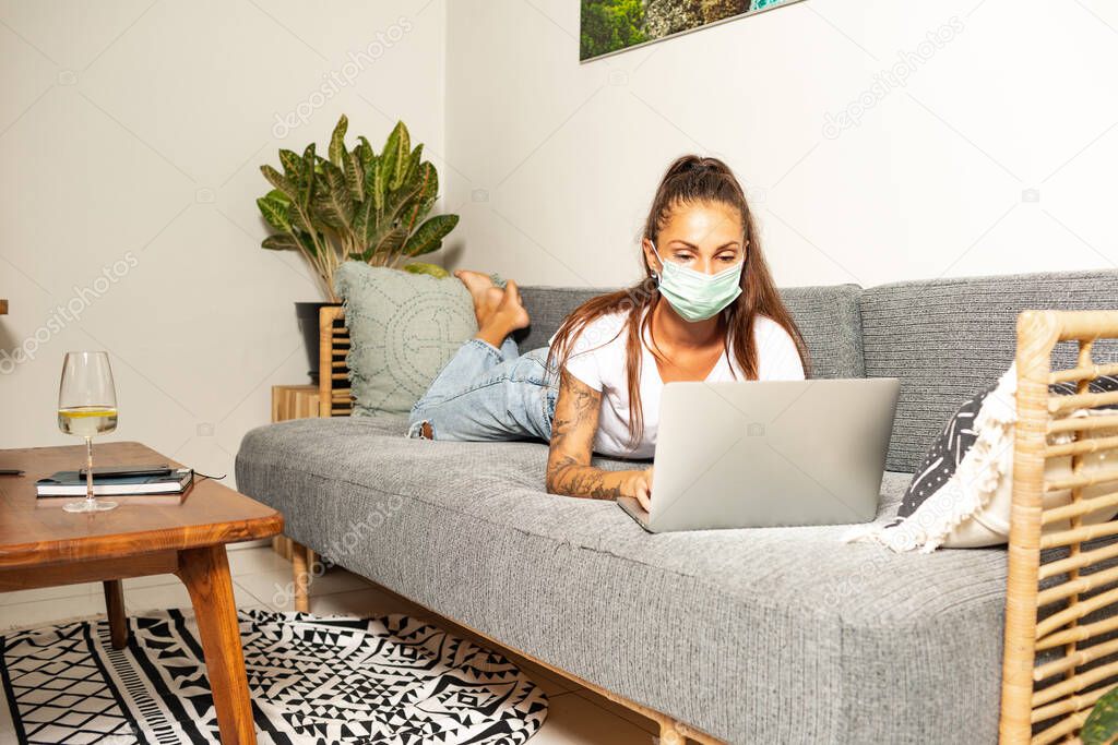 young woman working at home in face mask in room sofa background