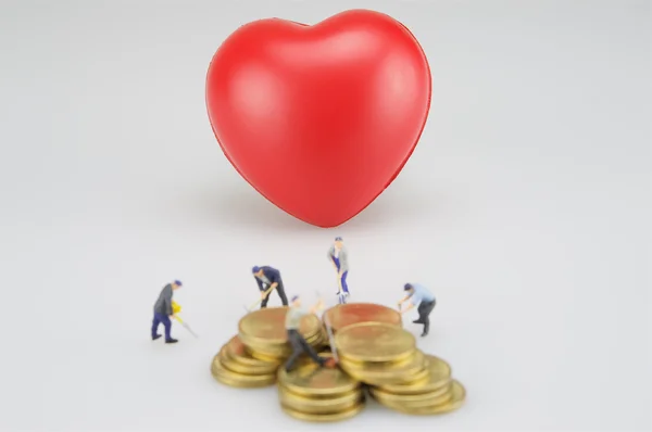 Corazón rojo y pilas de monedas borrosas con miniatura — Foto de Stock