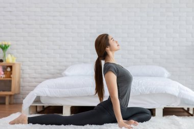 Çekici Asyalı kadın yoga güvercini pozu veriyor. Sabahları yatak odasında meditasyon yapıyor. Kendini çok rahat ve rahat hissediyor.