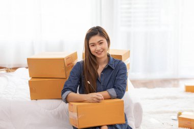 Laptop ile çalışan genç kadınların KOBİ girişimcisi ve evdeki sipariş çevrimiçi alışverişi için müşteri adresleri yazan Neşeli ve Mutlu, paket paketleri evde, başlangıç ve serbest konsepti ile birlikte