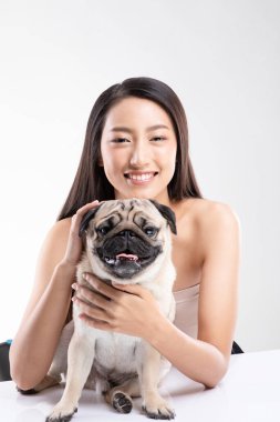 Güzel Asyalı kadın köpeğiyle gülümsüyor Pug, beyaz arka planda soyutlanmış, dost canlısı bir evcil hayvanla mutluluk üretiyor.
