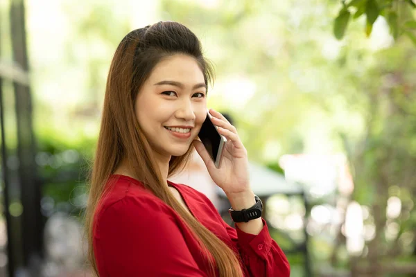ビジネスアジアの若い女性が赤いドレスを着て笑顔で働くとコーヒーショップでオフィス外での成功のためのアイデアや要件を得るためにスマートフォンで顧客と話をします 中小企業のコンセプト — ストック写真