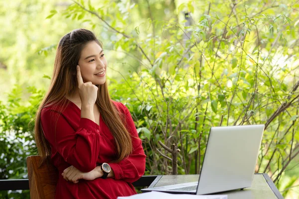 Business Asian young woman wearing red dress working with computer laptop and thinking to get ideas and requirement in Business startup feeling so happiness,Small Business Startup Concept