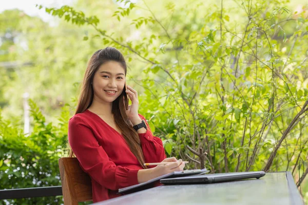 ビジネスアジアの女性は ノートパソコンの笑顔で作業し スマートフォンで顧客と話す赤いドレスを着て コーヒーショップでのオフィス外での成功のためのアイデアや要件を取得します 中小企業のコンセプト — ストック写真