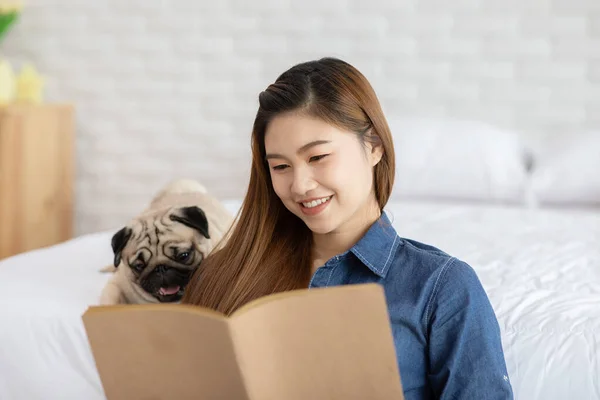 Atraente Asiático Jovem Mulher Ler Livro Enquanto Seu Cão Pug — Fotografia de Stock