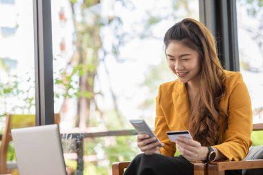 Güzel Çekici Asyalı kadın çevrimiçi alışveriş için kredi kartını kullanıyor çevrimiçi ödemeye dönüşüyor. Keyif ve mutluluk, alışveriş kavramı.