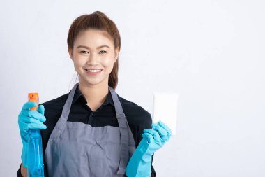 Çekici Asyalı Hizmetçi Kadın gülümsüyor ve daha temiz sprey ve sünger tutuyor. Mutluluk ve kendine güven hissediyor, beyaz arka planda izole edilmiş, Temizlik Hizmetleri Konsepti.